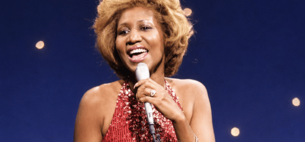 aretha franklin is singing "Something He Can Feel" from the film Sparkle on the tonight show with johnny carson in 1976. She has dirt blonde hair and is wearing a skin-tight, sleeveless red sequined and jewel-encrusted gown, holding a microphone in her left hand, with rings on both hands and a bracelet on her left hand