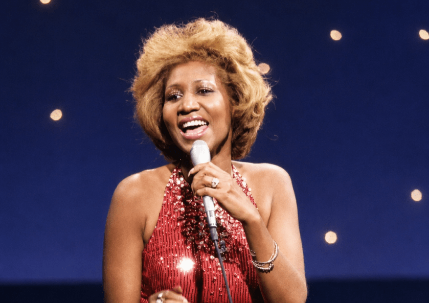 aretha franklin is singing "Something He Can Feel" from the film Sparkle on the tonight show with johnny carson in 1976. She has dirt blonde hair and is wearing a skin-tight, sleeveless red sequined and jewel-encrusted gown, holding a microphone in her left hand, with rings on both hands and a bracelet on her left hand